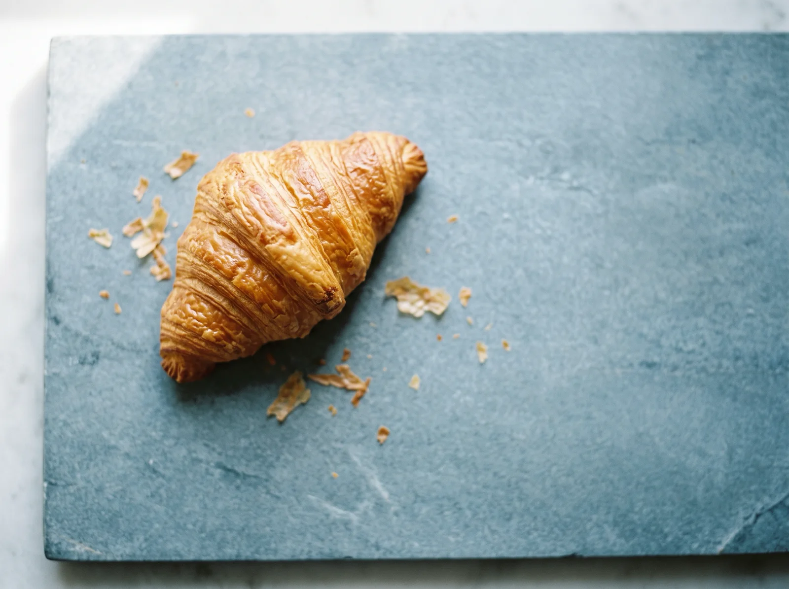 Croissant on a Cool Blue-Gray Slab from Above — AI-generated photograph