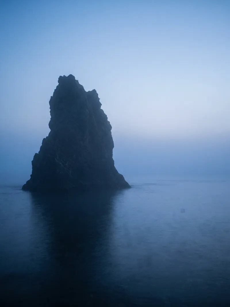 Lone Sea Stack in Blue Sea Fog — AI-generated photograph