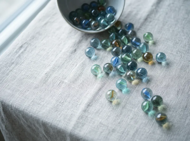 Overhead Glass Marbles Scattered on Pale Linen — AI-generated photograph
